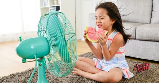 A young girl sitting in front of a fan on a hot day.