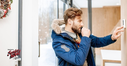 An adult man adjusting his thermostat in his house.